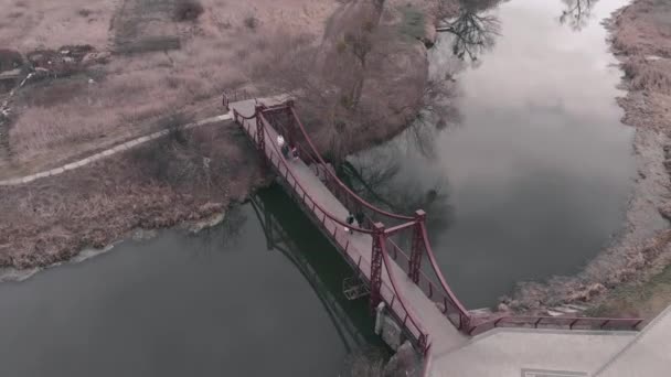 Puente peatonal a través del río con paseo marítimo y parque, vista aérea. Drone volando sobre muelle de la ciudad con poco río y bosque — Vídeo de stock