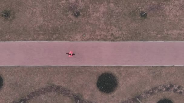 Mulher está correndo no caminho pedestre vazio. Atleta feminina em roupas esportivas brilhantes corre ao longo da estrada pedonal, vista aérea superior — Vídeo de Stock