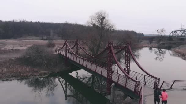 Sportive couple running on bridge. Man and woman jogging in park with river and bridge. Female and male athletes run in recreation area — Stock Video