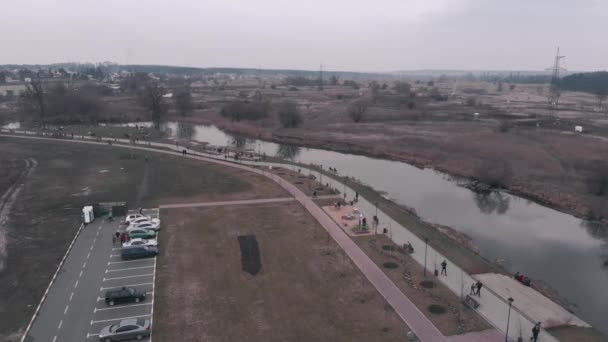 Πεζόδρομος χώρος αναψυχής με ποτάμι και χώρο στάθμευσης αυτοκινήτων από τα πουλιά με θέα στα μάτια. Αεροφωτογραφία drone του πάρκου με τους ανθρώπους που περπατούν κατά μήκος περιπάτου — Αρχείο Βίντεο