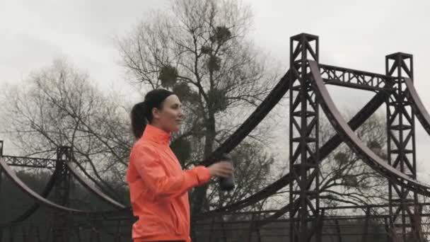 Atleta feminina esportiva em roupas esportivas brilhantes bebendo água da garrafa. Jovem morena bebe água durante o treinamento de corrida. Conceito de desporto — Vídeo de Stock