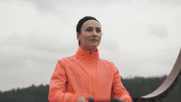 Kvinna i ljusa sportkläder sätter på hörlurar innan träning utomhus. Ung kvinnlig idrottsman sätter på svarta stora hörlurar i parken. Idrott och löpning — Stockvideo