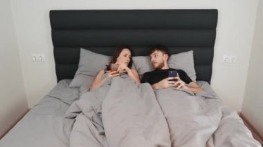 Genç bir çift yatakta yatıyor, kadınlar kocalarının akıllı telefonlarına bakıyor. İlişkide kriz. Kadın ve erkek yatakta uzanıyor ve akıllı telefonlara bakıyor, iletişim ağı içinde..