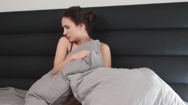Пригнічена самотня жінка на самоті в ліжку. Молода біла сумна жінка сидить на порожньому сірому ліжку вдома — стокове відео