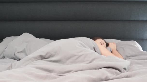 Женщина спит в постели одна, во времени. Молодая брюнетка-кавказка спит на пустой серой кровати . — стоковое видео