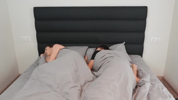 Мужчина обнимает лежащую в постели женщину. Молодая семейная пара лежит в спальне. Обиженная жена лежит в постели рядом с мужем. Кризис в отношениях — стоковое видео