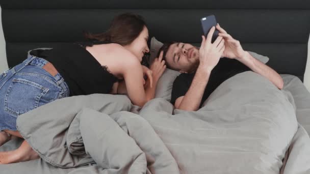 Elbűvölő barna feleség flörtöl a fiatal férjével az ágyban. A fiatal vonzó nő flörtöl az ágyban fekvő férfival. Boldog házaspár pihennek az ágyban — Stock videók