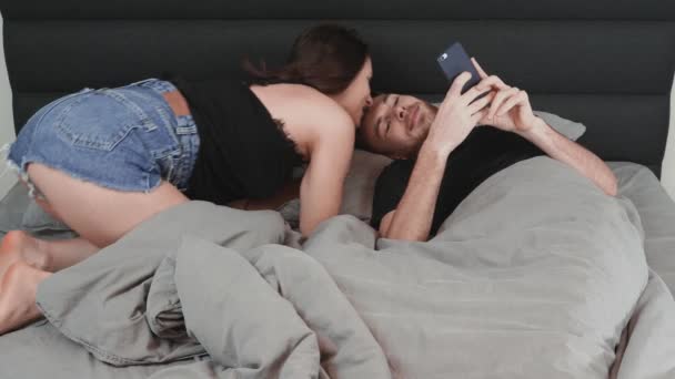 Glückliches Ehepaar, das im Bett liegt und miteinander flirtet. Die junge charmante Frau flirtet mit ihrem Mann im Bett. Attraktive charmante Frau flirtet mit Mann zu Hause — Stockvideo