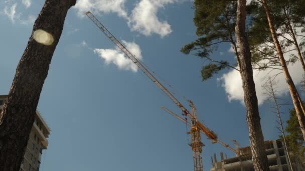 Guindaste alto trabalha no local de construção com uma casa. Construir os edifícios. Processo de construção de arranha-céus com guindastes contra o céu azul com nuvens, lapso de tempo . — Vídeo de Stock