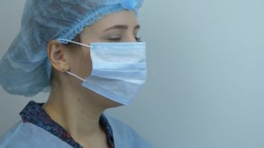 Koruyucu tıbbi maskesini çıkaran kadının portresi, yakın çekim. Genç kadın bilim adamı tıbbi mavi maskeyi çıkarıyor. Doktor ameliyat sonrası koruyucu yüz maskesini çıkarıyor.