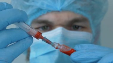 Coronavirus aşısı. 2019-nCoV COVID virüsü için önleyici ilaçlar içeren koruyucu tıbbi malzemeler taşıyan bir erkek. Doktor enjeksiyon için şırıngayı ilaçlarla doldurur.