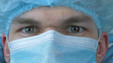 Erkek doktor, cerrahi tedaviden önce koruyucu bir yüz maskesi takar. Tıbbi koruyucu giysili bir adam ameliyata hazırlanıyor. Tıbbi maske takmış beyaz bir adamın portresi. Virüs koruması.