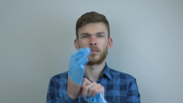Молодой кавказский мужчина надевает медицинские перчатки для профилактики и защиты от вирусной инфекции. Мужчина в латексных медицинских перчатках для пандемической защиты коронавируса Ковид-19 — стоковое видео