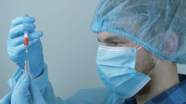 Вакцинация коронавирусом. Мужчина-лаборант в защитном медицинском снаряжении держит шприц с профилактическими препаратами для инъекции вируса COVID 2019-nCoV. Человек наполняет шприц лекарствами для инъекций — стоковое видео