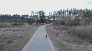 Bisikletçi pedalları hızlı ve yoğun bir şekilde çam ağacı ormanındaki boş otoyolda bisiklet sürüyor. Sadece bisiklete binen sporcuların hava görüşü. Ormanda tek başına bisiklete binmek. Triatloncu sert pedal çeviriyor.