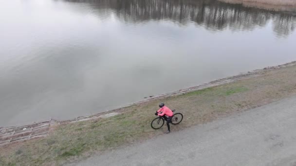 Radprofi auf Rennrad steht in der Nähe des Großen Sees. Draufsicht auf Triathleten, die sich auf das Radtraining vorbereiten. Frau mit Helm und Fahrradkleidung steht mit Fahrrad und blickt auf Damm. Sportkonzept — Stockvideo