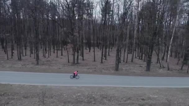 Woman in helmet cycling on road bike on empty car road in forest. Cyclist riding fast on isolated highway in woodland. Triathlete pedals intensively on bicycle alone. Athlete preparing for bike race — Stock Video