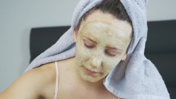 Mujer afeitándose las piernas en la cama con tiras de cera y sintiendo dolor. Mujer con mascarilla facial y toalla en la cabeza haciendo depilación. Primer plano de la cara de la mujer sintiendo dolor durante la depilación — Vídeo de stock