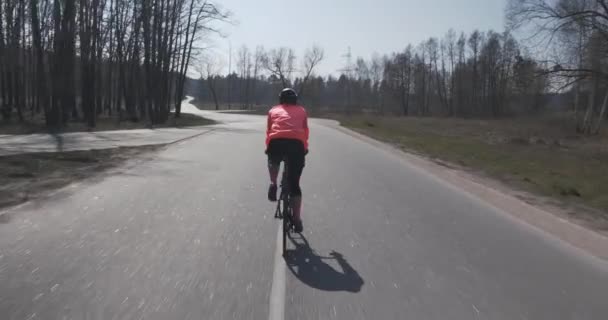 自転車に集中してペダルを漕ぐ女性。ヘルメットを被った女性選手が自転車に乗っている。空の道をサイクリングする少女アスリート。トライアスロンのコンセプト — ストック動画