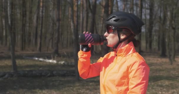 Kobieta w kasku i okularach pije wodę z butelki. Portret rowerzystki pijącej izotoniczny napój. Zamknij dziewczynę z butelką przed treningiem. Koncepcja kolarstwa i triatlonu — Wideo stockowe