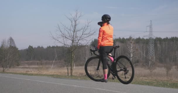 Женщина пьет воду и готовится к поездке на велосипеде. Женщина-велосипедистка в шлеме пьет из бутылки и начинает тренироваться на велосипеде. Девушка перед поездкой тренировки. Концепция велоспорта и триатлона — стоковое видео