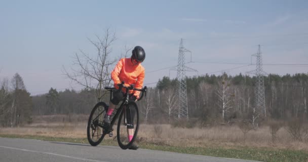 Велосипедист п'є з пляшки перед поїздкою. Жінка в шоломі та велосипедному одязі питна вода. Портрет жінки з дорожнім велосипедом на відкритому повітрі. Концепція велоспорту та тріатлону — стокове відео