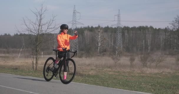 Жінка-велосипедистка бере селфі по телефону. Жінка на велосипеді робить фотографії на смартфоні. Дівчина в шоломі з шоломом робить фотографії. Концепція спорту та способу життя — стокове відео