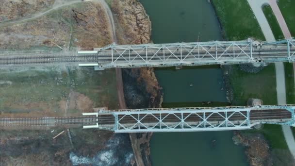 Металлический железнодорожный мост через реку, вид сверху с воздуха. Смотрю вниз на высокоскоростные железнодорожные линии. Пустые железные дороги через узкую реку — стоковое видео