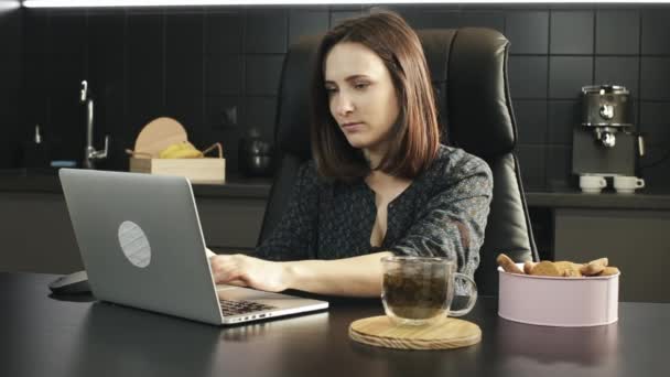 La mujer trabaja en la computadora portátil en casa. Retrato de mujer de negocios usando portátil en la cocina. Joven mujer escribiendo en el teclado portátil y estiramiento durante el trabajo en el portátil en casa — Vídeos de Stock