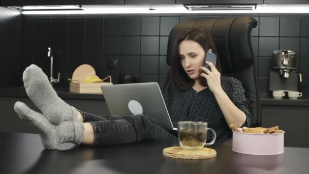 Mujer haciendo una llamada amistosa desde casa. Joven freelancer trabajando ordenador portátil desde casa y hablando en smartphone. Chica hablando con el contacto comercial o amigo en el lugar de trabajo en casa — Vídeos de Stock