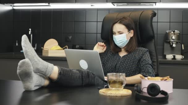 自宅の職場からビデオ通話会議を作る保護医療面の少女。自宅で保護顔マスクを身に着けている女性。自宅のノートパソコンで医療用マスクをしている女性 — ストック動画