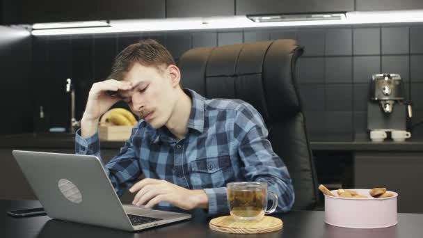 Zmartwiony męski wolny strzelec z bólem głowy pracujący na laptopie w domu. Zdenerwowany człowiek pracujący nad notatnikiem w kuchni. Nieszczęśliwy człowiek korzysta z technologii komputerowej w domu. Smutny człowiek patrzący na ekran laptopa — Wideo stockowe
