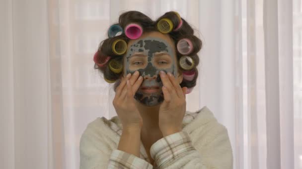 Mujer haciendo procedimientos de cosmetología en casa. Rutina de belleza femenina en casa. Máscara de mujer. Chica con máscara de piel cosmética en la cara. Cuidado de la piel. Belleza y cosmetología. Máscara de carbón o barro de barro negro — Vídeos de Stock