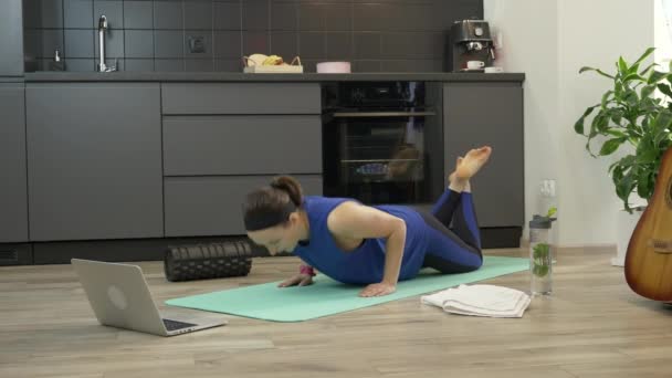 Silna pewna siebie dziewczyna robi ćwiczenia push up w domu w kuchni. Piękna kobieta fitness w odzieży sportowej o treningu online w domu za pomocą aplikacji na notebooku. Kobieta wykonująca ćwiczenia aerobowe — Wideo stockowe