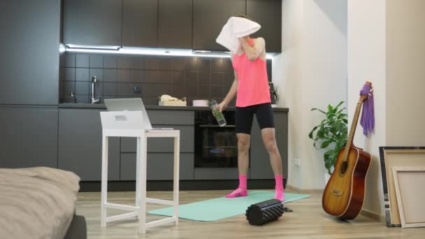 Joven hombre caucásico en ropa deportiva rosa beber agua después de entrenamiento de fitness en línea en casa. Divertido atleta masculino de 80 limpiando la cara con una toalla después del entrenamiento aeróbico. Concepto de deporte doméstico — Vídeo de stock