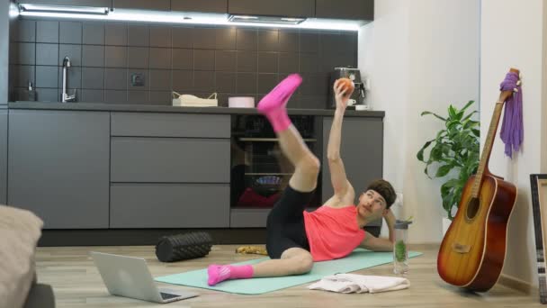 Férfi csinál fitness és aerobic gyakorlatok otthon a konyhában segítségével online képzési alkalmazás laptop számítógépen. Vicces férfi rózsaszín sportruhában, reggeli gyakorlatokat végez otthon a karantén alatt. — Stock videók