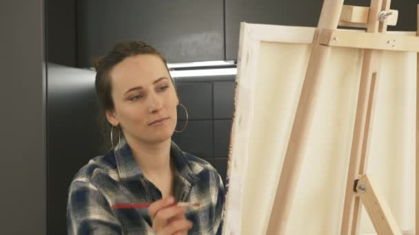 Jeune artiste féminine dessin image sur toile dans la cuisine moderne à la maison. Thérapie d'art domestique. Inspiration. Femme talentueuse peinture tableau sur chevalet à l'aide de peintures acryliques — Video