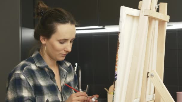 Yetenekli yenilikçi kadın sanatçı evdeki modern mutfakta tuvale resim çiziyor. Ressam soyut modern sanat yaratıyor. Esmer kadın resim çiziyor ve gülümsüyor. Evde sanat terapisi gören bir kız. — Stok video