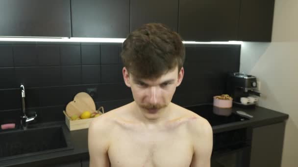 Portrait of young naked caucasian man with mustache in kitchen at home, looking to camera and smiling. Young hipster smiling male with mustache looking at camera, front view. — Stock Video