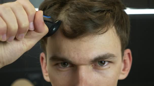 O rosto masculino jovem rapa o cabelo com o barbeador elétrico, de perto. Cabeça de barbear homem com cortador elétrico em casa — Vídeo de Stock