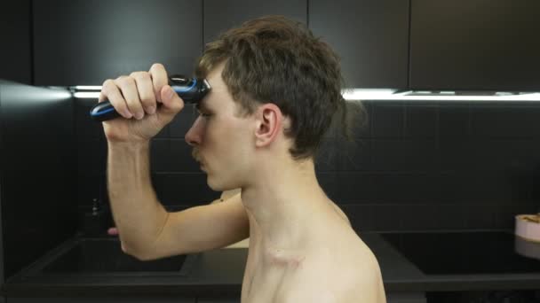 Człowiek golił głowę elektrycznym trymerem z powodu izolacji podczas kwarantanny koronawirusowej. młody kaukaski mężczyzna goli głowa z elektryczny brzytwa w domu — Wideo stockowe