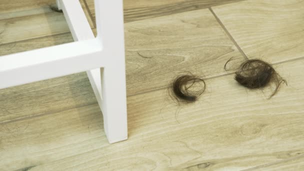 美容室の床に髪をカット。ヘアサロンに落ちる茶色の髪をカットします。短い黒い髪は床に落ちる。床に落ちる髪 — ストック動画