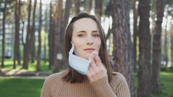 Retrato de una mujer joven quitándose la mascarilla médica protectora, respirando aire fresco y sonriendo en la calle. Coronavirus covid-19 en cuarentena. Protección contra infecciones virales. Prevención de epidemias — Vídeo de stock