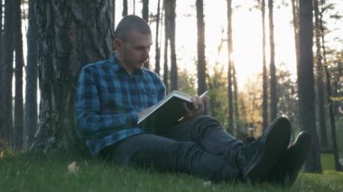 Kamu parkında çimlerde oturan ve gün batımında kitap okuyan bir erkek öğrenci. Parkta ders çalışan, edebiyat okuyan ve günbatımının tadını çıkaran genç bir öğrencinin portresi. Mutlu insanlar kavramı