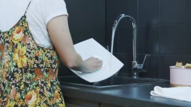 Kadın elleri mutfak lavabosunda tabağı süngerle ve temizleyiciyle yıkıyor. Evde ev işi yapan bir kadın. Kadın elleri modern mutfak lavabosunda bulaşık yıkıyor. Ev işi ve temizlik konsepti