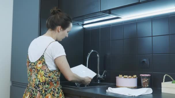 Female washes dish in modern kitchen sink. Woman rinses plate in kitchen sink. Woman washes plate with her hands at the kitchen sink under stream of water — Stock Video