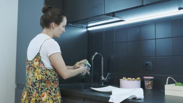 Vidro de lavagem feminino com esponja e limpador na pia da cozinha. Mulher a limpar cozinha. A dona de casa lava pratos na pia de cozinha abaixo da água de fluxo. Conceito de limpeza da casa — Vídeo de Stock