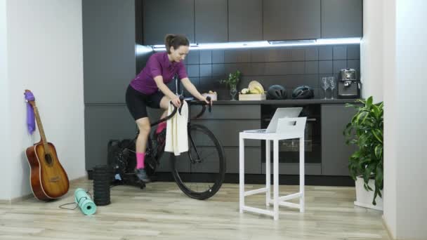 Kobieta jeżdżąca na rowerze stacjonarnym. Dziewczyna robi fitness cardio trening na krytym inteligentnym rowerze trener pobyt w domu podczas pandemii koronawirusa dla dystansu społecznego samodzielne odizolowane w kwarantannie — Wideo stockowe
