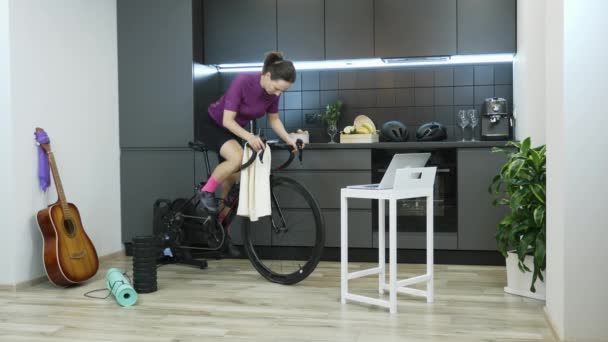 Cykling kvinna gör sport övningar på smart tränare stannar hemma under coronavirus pandemi för social distancing själv isolerad i karantän. Kvinnlig utbildning på cykel tittar på datorskärm — Stockvideo