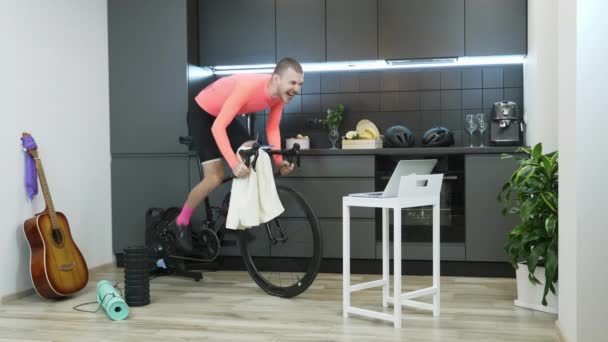 Killen trampar intensivt på stationär cykel hemma och sprintar. Ung man idrottsman deltar i online cykling tävlingar stannar hemma under karantän av coronavirus. Självförvållande. Idrottsbegreppet — Stockvideo